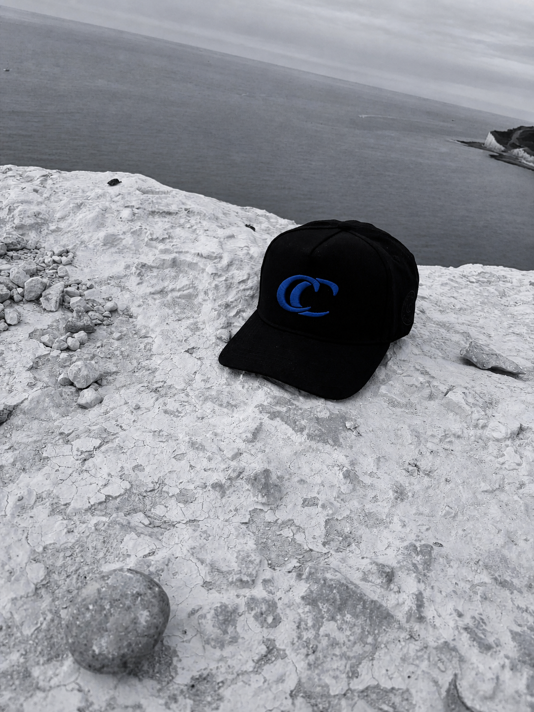 Black CC Essential Cap photographed on a monochrome coastal cliff